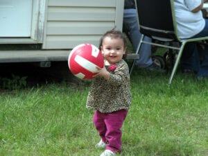 A little girl holding onto a ball in the grass.