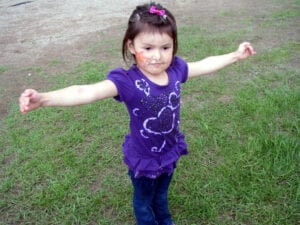 A little girl standing in the grass with her arms outstretched.