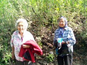 Two older women standing next to a bush.