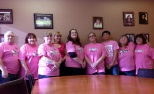 A group of people wearing pink shirts and standing around a table.